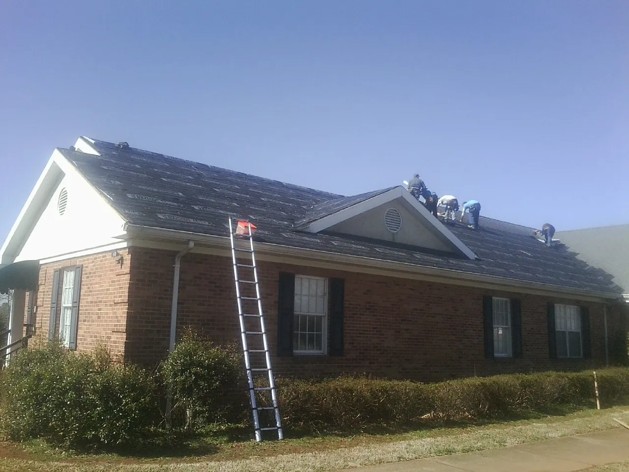 Crew tearing shingles off a brick ranch roof with a ladder set — Emergency Roof Repair work by our crew in Livingston