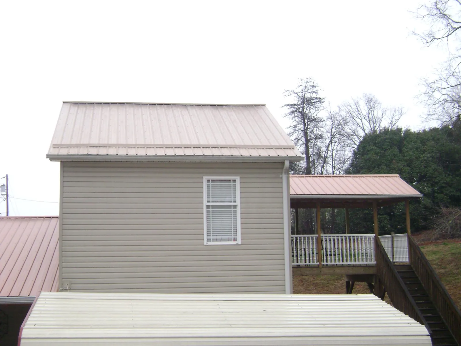 Tan metal roofs on a two story addition and attached porch, from a Roof Replacement job in Livingston